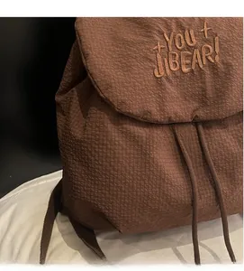 Close-up of brown nylon backpack featuring grid texture fabric and letter embroidery