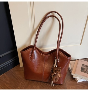 Macro shot of large caramel brown tote bag with glossy texture and teddy bear charm