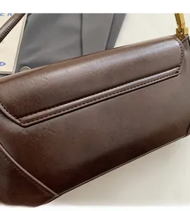 Detail of dark brown leather baguette bag with matte texture and golden buckle fastener