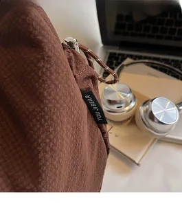 Nahaufnahme der braunen Canvas-Tasche mit Waffelstruktur, Markenlabel und Metallreißverschluss