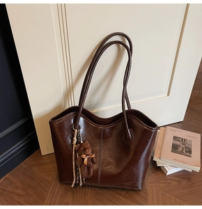 Detail of dark brown glossy tote bag with teddy bear charm on wooden floor