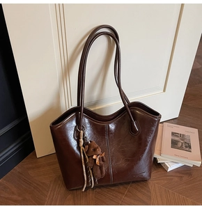 Close-up of a dark brown large tote bag in glossy oil wax leather with a bear pendant