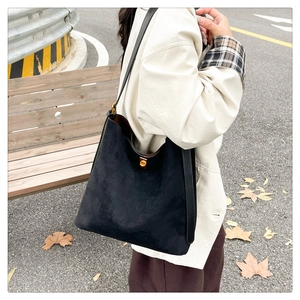 Detail shot of black suede tote bag with gold metal buckle shown on an outdoor wooden bench