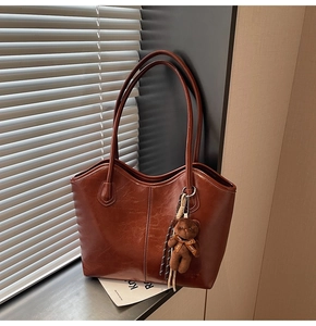 Detailed view of large brown tote bag with glossy leather texture and cute plush bear charm