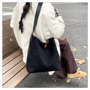 Back view of a black suede tote bag with a gold metal twist lock in a scenic outdoor setting