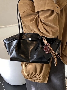 Glossy black tote bag with silver buckle and leopard heart charm shown on shoulder