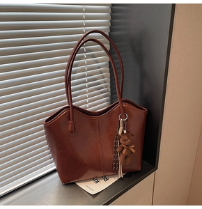 Detail of dark brown tote bag with glossy leather texture and cute bear charm hanging