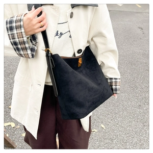 Detail of black suede tote bag with golden metal twist-lock and leather shoulder strap