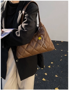 Brown quilted tote bag with yellow smiley charm shown over-the-shoulder on model