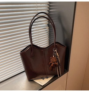 Detail of dark brown leather tote bag with plush bear charm and woven rope accessory