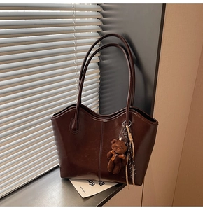 Detail of dark brown leather tote bag with wavy top edge and cute plush bear charm