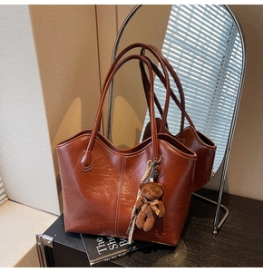 Detail of glossy brown leather tote bag with plush bear charm and textured finish