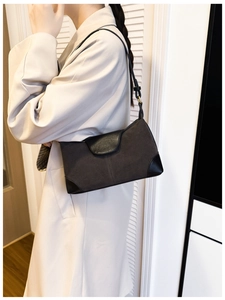 Detail of suede and black leather shoulder bag styled with a beige trench coat