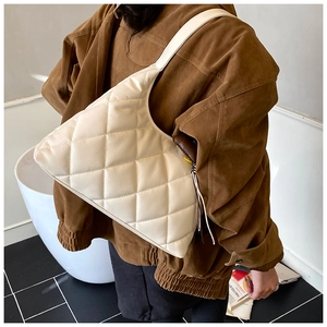 Close-up of beige quilted shoulder bag with diamond stitching on a matte leather surface