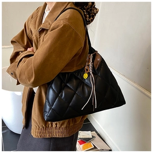 Close-up of black quilted tote bag with yellow smiley face and woven rope charms