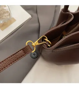 Detailed close-up of dark brown leather bucket bag with high-shine gold metal lobster clasp