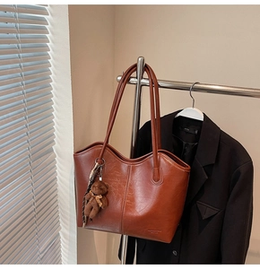 Detail of red-brown faux leather tote bag featuring a cute plush bear charm on a metal hanger