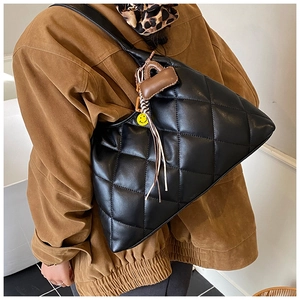 Detail of black quilted shoulder bag featuring letter D charm and yellow smiley face tag