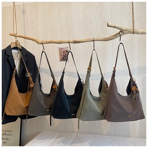 Minimalistische suède-look tassen in vijf kleuren hangend aan een houten tak