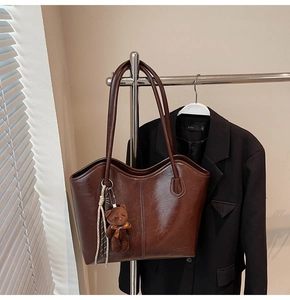 Detail of a brown leather tote bag with a small bear pendant and textured finish