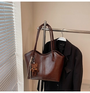 Detail of dark brown tote bag with polished leather finish and cute plush bear charm
