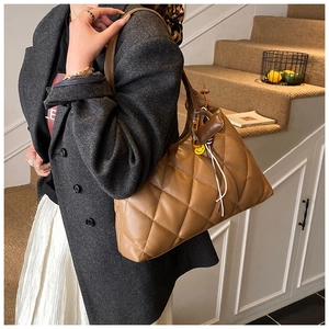 Detailed view of brown quilted faux leather shoulder bag with yellow smiley face pendant