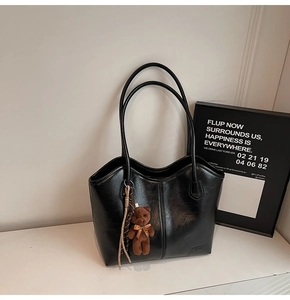 Close-up of black leather tote bag with vertical stitching and brown teddy bear charm