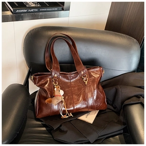 Dettaglio borsa tote vintage marrone scuro con ciondolo a cavallo su divano in pelle