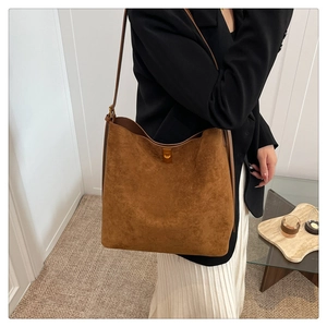 Brown suede hobo tote bag with gold buckle on shoulder of model in minimalist setting