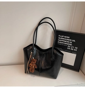 Detail of black glossy leather tote bag with a cute plush bear charm on white desk