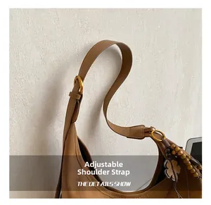 Detail van verstelbare leren riem met gouden gesp en kralenhanger aan bruine tas