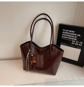 Detail of dark brown wax leather tote bag with vertical stitching and plush bear charm