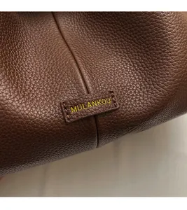 Detail of lychee pattern leather and MULANKOU brand logo on a brown bucket bag