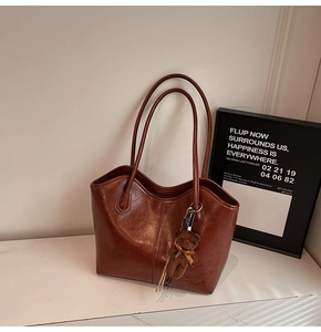 Detail of vintage brown leather tote bag with plush bear charm and tassel on white marble