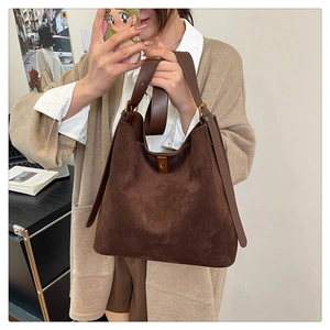 Detail of a deep brown brushed suede tote bag featuring a gold buckle and leather handle