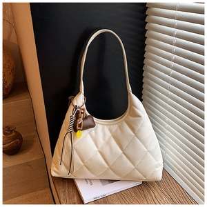 Close-up of quilted cream shoulder bag featuring decorative heart and tassel charms