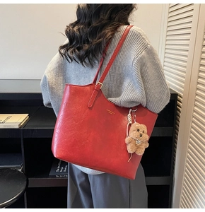 Detail of red pebbled leather tote bag featuring golden hardware and a cute plush bear charm