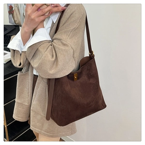 Detail of dark brown suede tote bag with gold twist lock on beige knit cardigan