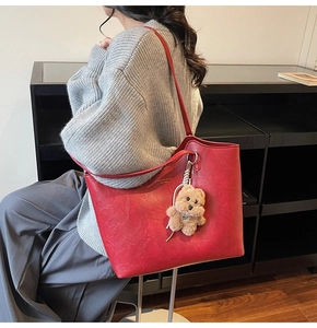Close-up of red leather tote bag with fashion text and a cute brown plush bear charm