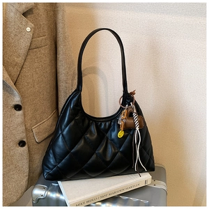 Close-up of black quilted shoulder bag with heart and tassel charms on a beige coat background