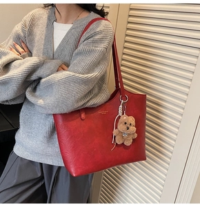 Detail of red leather tote bag with gold lettering and cute brown plush bear charm