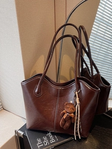 Brown vintage faux leather tote bag with plush bear charm on a book background
