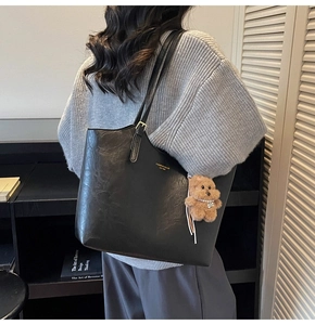 Close-up of black tote bag with gold lettering and a cute brown teddy bear charm
