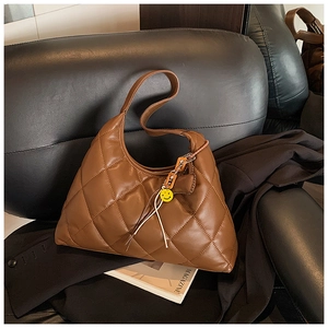 Detail of dark brown quilted hobo bag with yellow smiley face charm on a black sofa