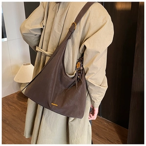 Detail of dark brown leather tote bag with wide strap and tassel worn with trench coat