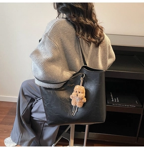 Detail of black matte leather tote bag with FASHION & BAGS text and brown bear charm