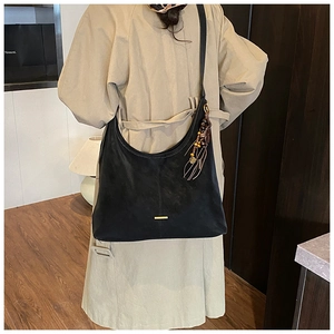 Close-up of black suede hobo bag with golden hardware and tassel charm on model