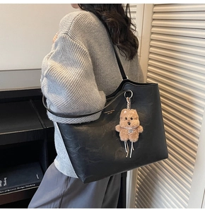 Detail of black tote bag with plush bear charm and textured leather for daily commute