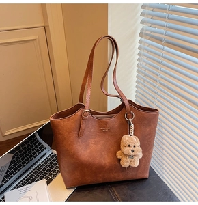 Close-up of vintage brown leather tote bag with stylish bear pendant on a desk