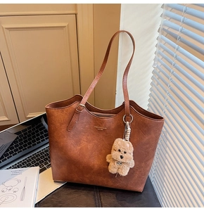 Detail of dark brown leather tote bag with vintage texture and cute plush bear charm